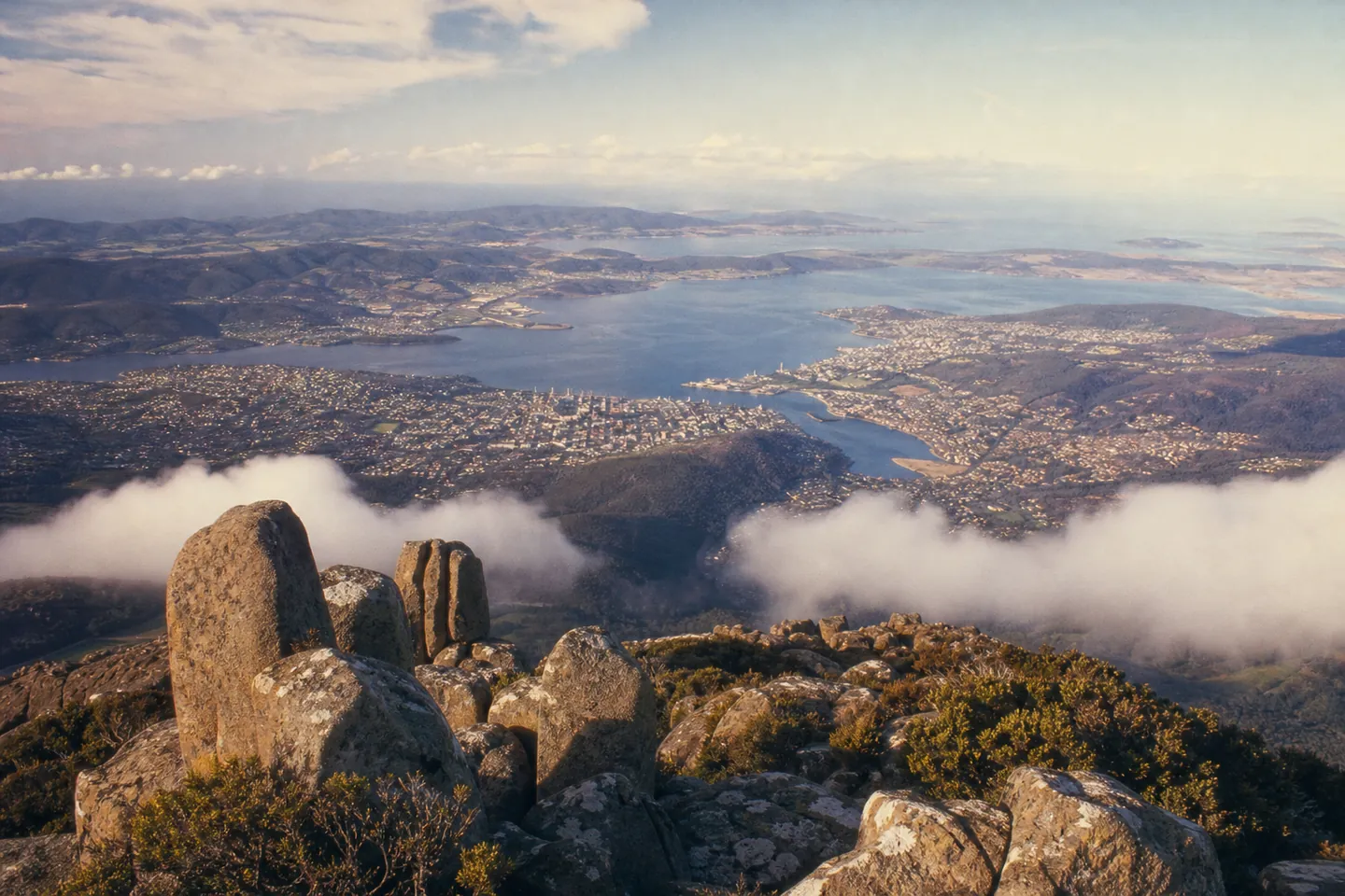 Illustration: view from a rocky mountain summit over a city on a wide river estuary